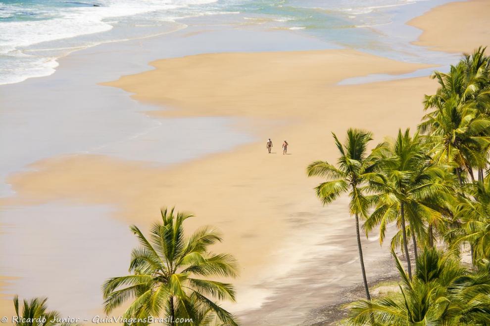 Imagem do alto de duas pessoas caminhando na praia.